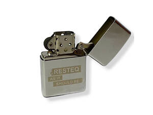 Классическая бензиновая зажигалка типа Зиппо с надписью 'RESTEQ AS IT SHOULD BE'. Многоразовая зажигалка